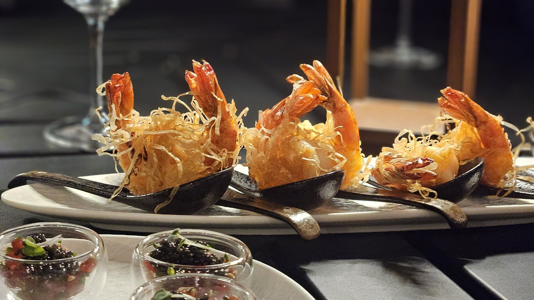 Crispy kadaif-wrapped prawns on black spoons.